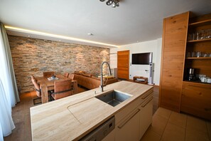 A modern kitchen with a stone wall, wooden cabinets, and a dining area with leather seating. - Zell City Exclusive Lodges: Top 3, Balcony (Zell am See)