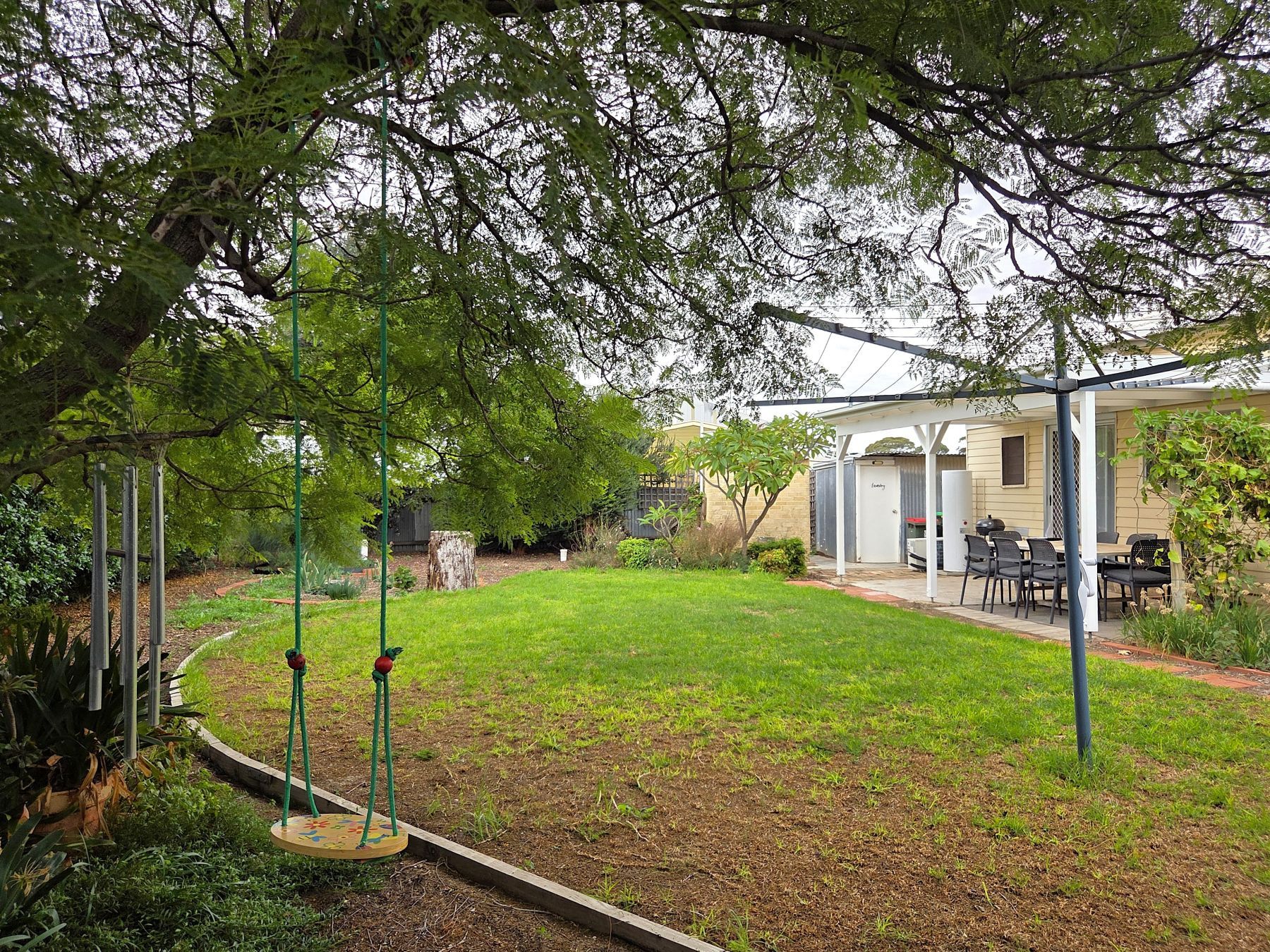 A backyard with a swing set, a covered patio area, and a lawn.