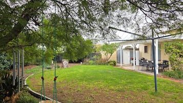 A backyard with a swing set, a covered patio area, and a lawn.