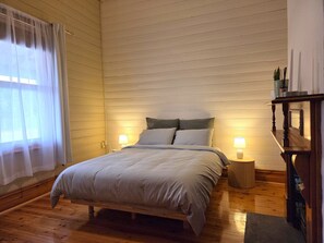 A bedroom with a wooden bed, two bedside lamps, a nightstand, and a window with sheer curtains.