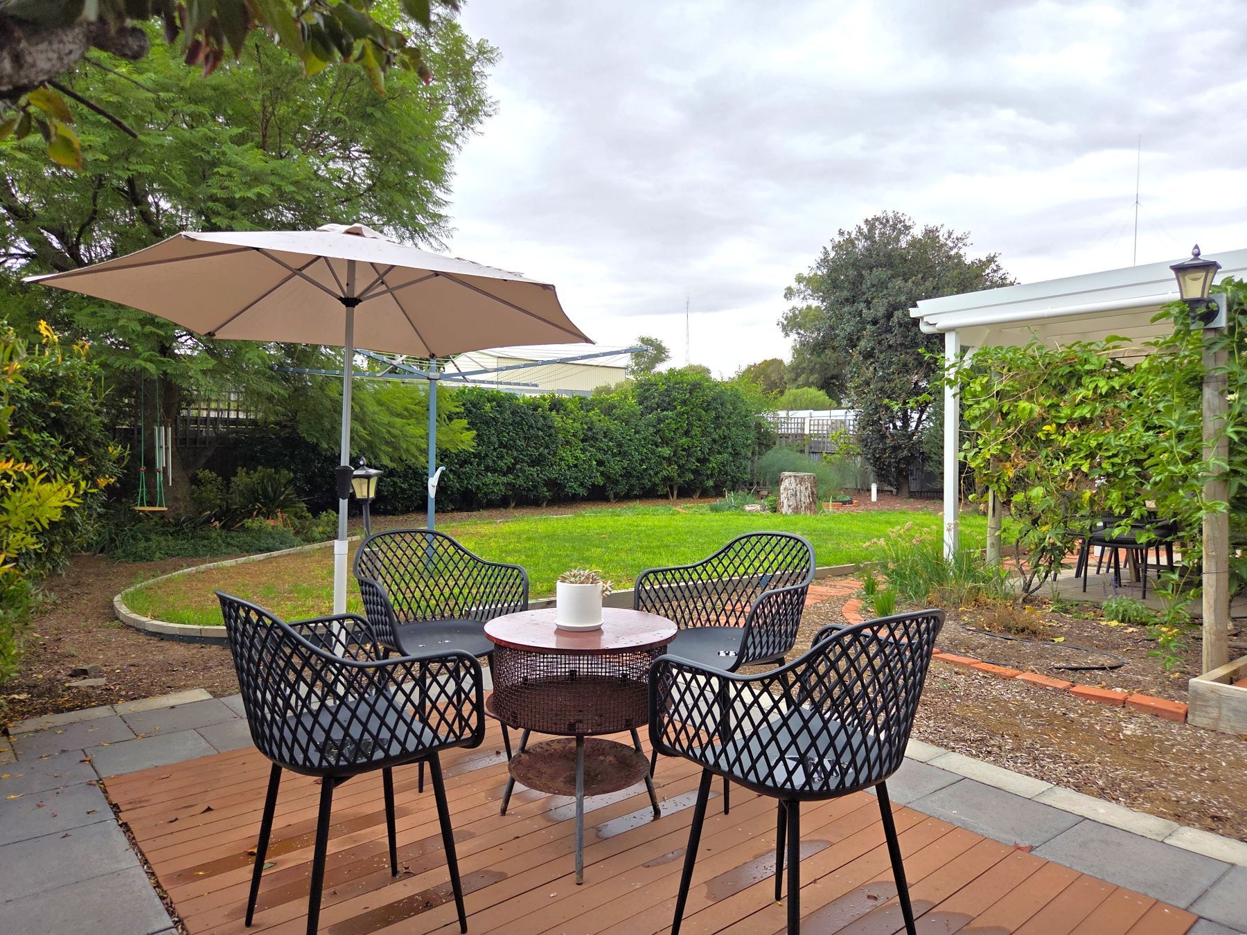 An outdoor patio with a round table and chairs, a large umbrella, and a garden view.