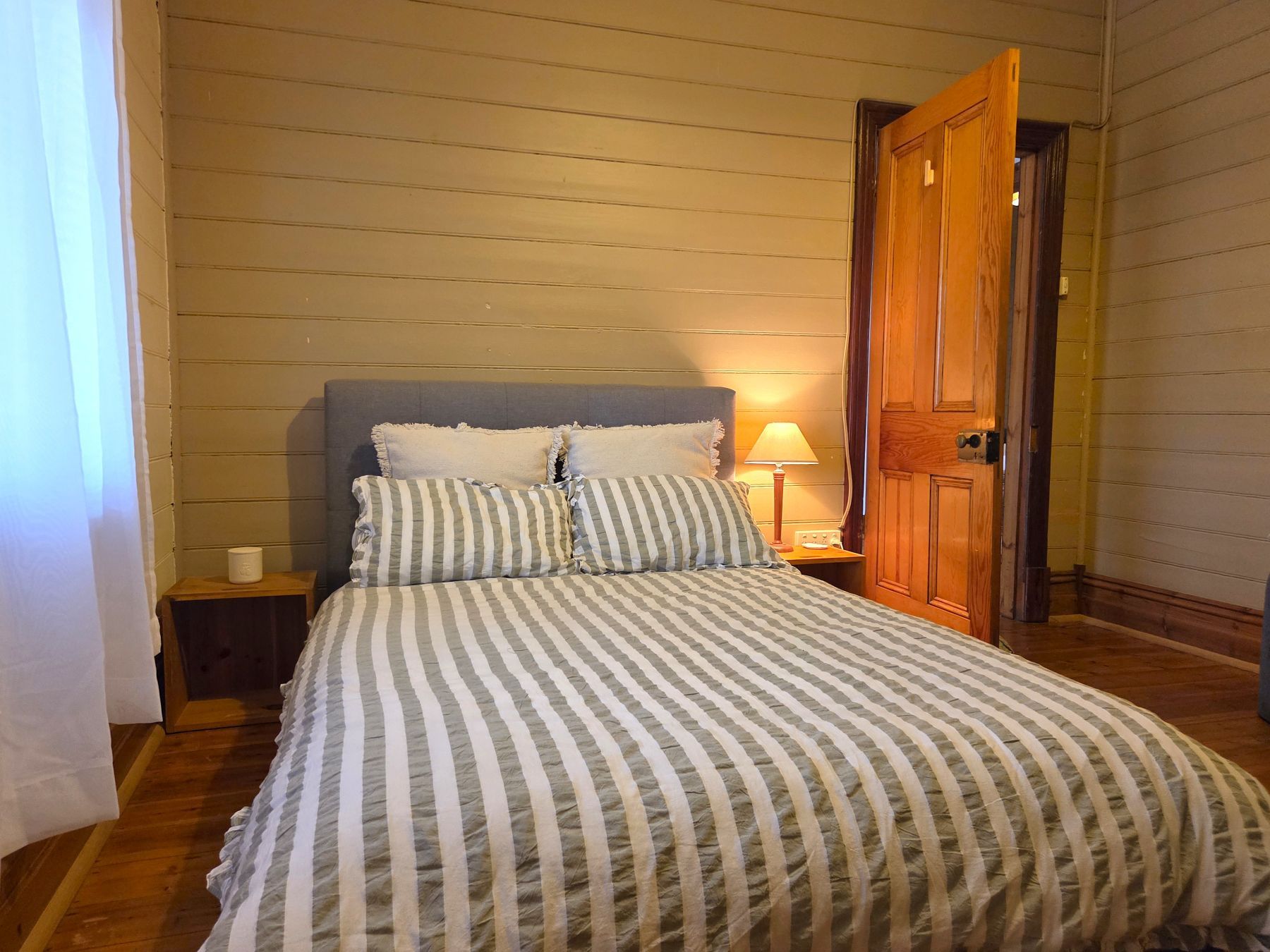 A bedroom with a bed, a nightstand, a lamp, and a wooden door.