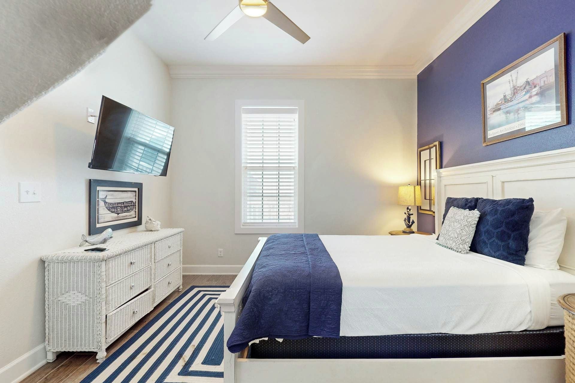 A bedroom with a bed, a dresser, a television, a window, and a painting on the wall.
