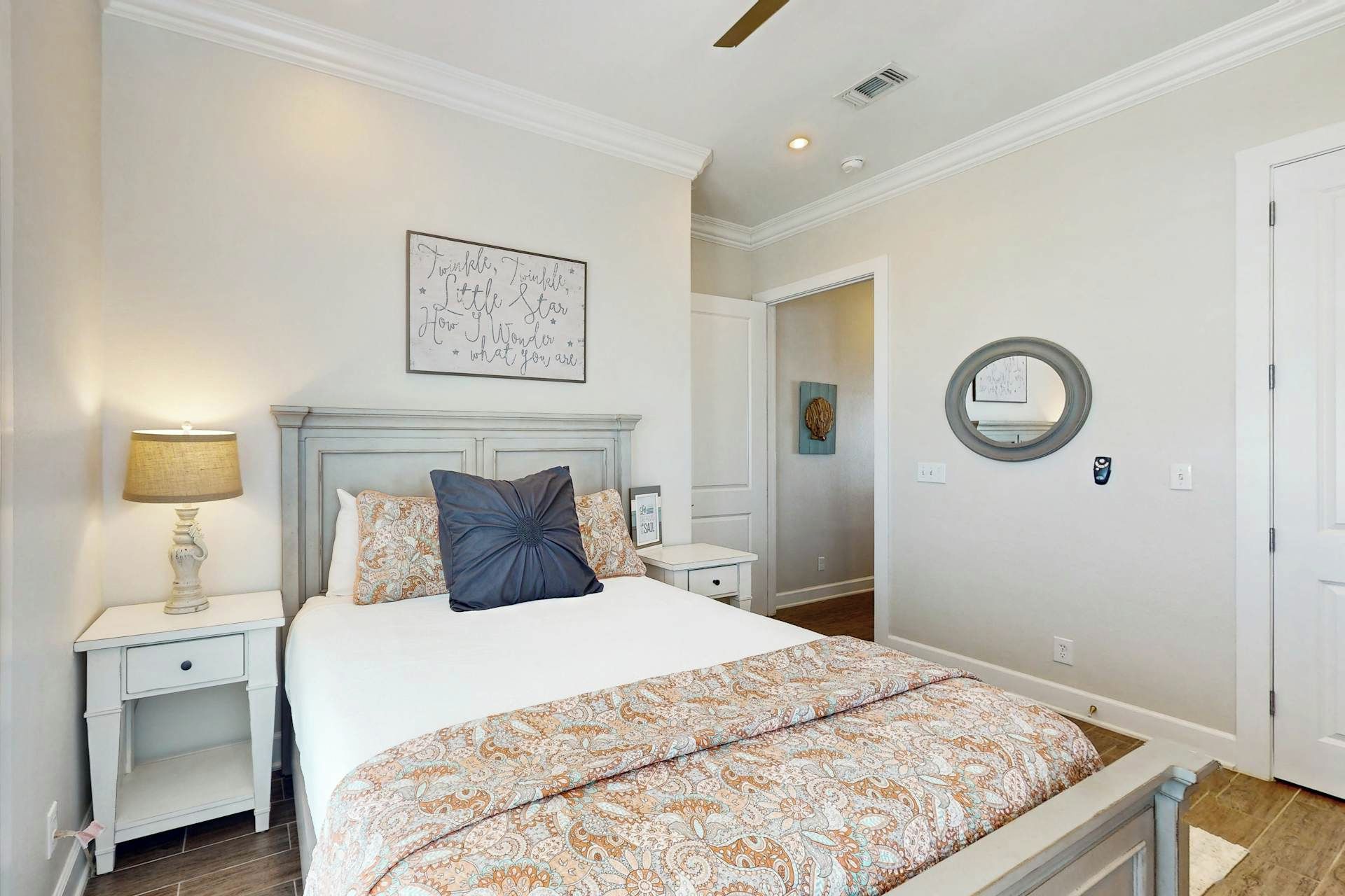 Un dormitorio con cama, mesitas de noche, un espejo en la pared y un letrero decorativo.