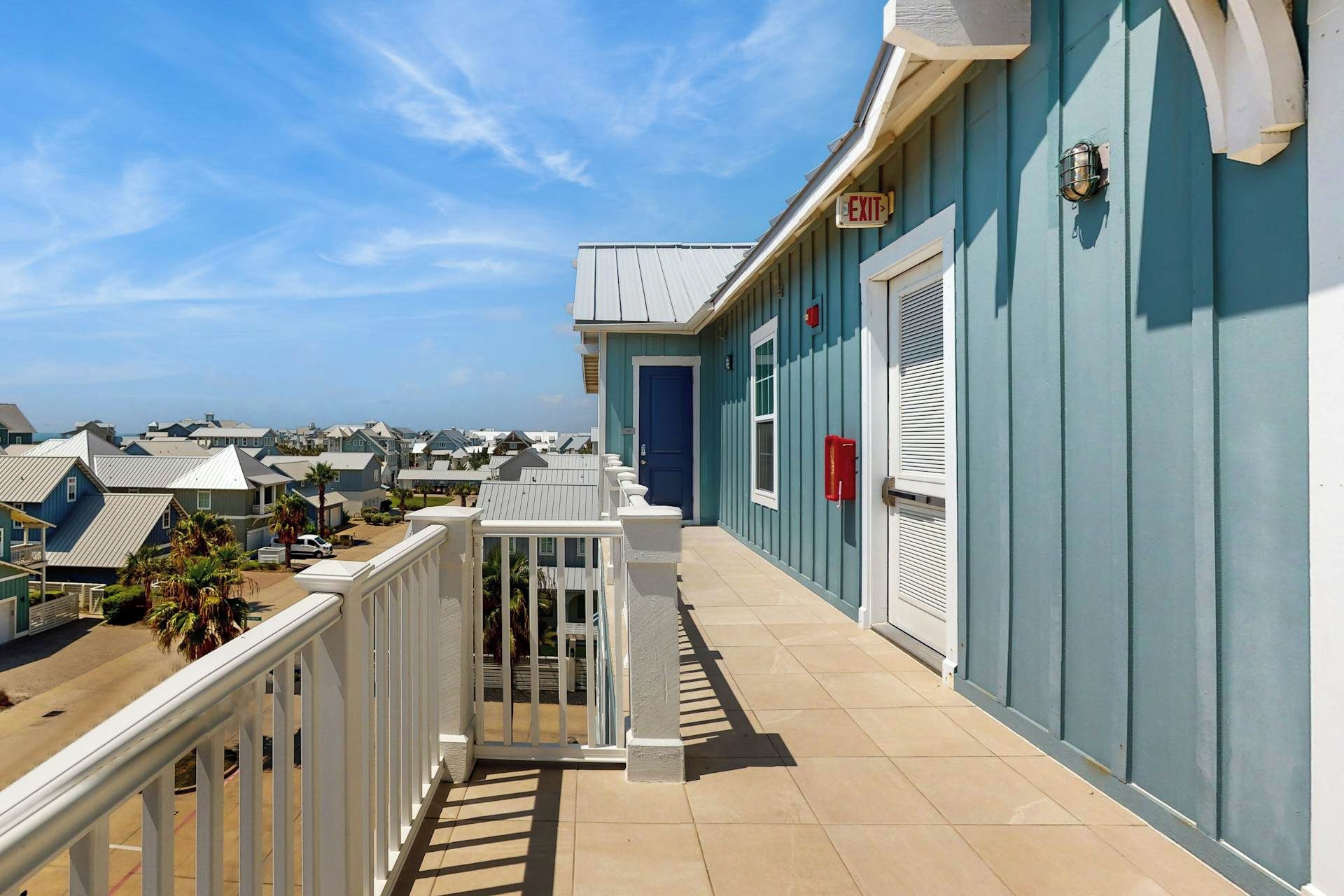 Un balcon avec une balustrade blanche, une porte bleue et un panneau de signalisation rouge indiquant la sortie.