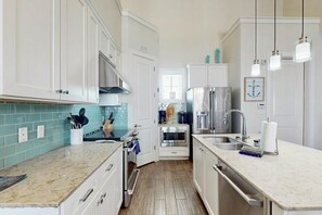 A modern kitchen with white cabinetry, a tiled backsplash, stainless steel appliances, and pendant lighting. - Pet-Friendly | Water Views | Steps to Beach (Port Aransas)