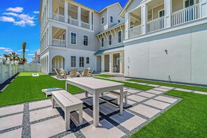 A two-story building with a covered patio area, outdoor seating, and a well-maintained lawn. - Palmilla's Sunset | Pet Friendly | Steps to Beach (Port Aransas)