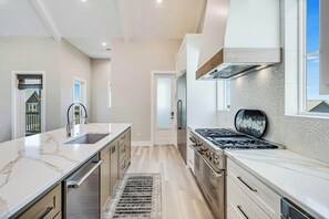 A modern kitchen with a marble countertop, stainless steel appliances, and a view of the outside. - Palmilla's Sunset | Pet Friendly | Steps to Beach (Port Aransas)