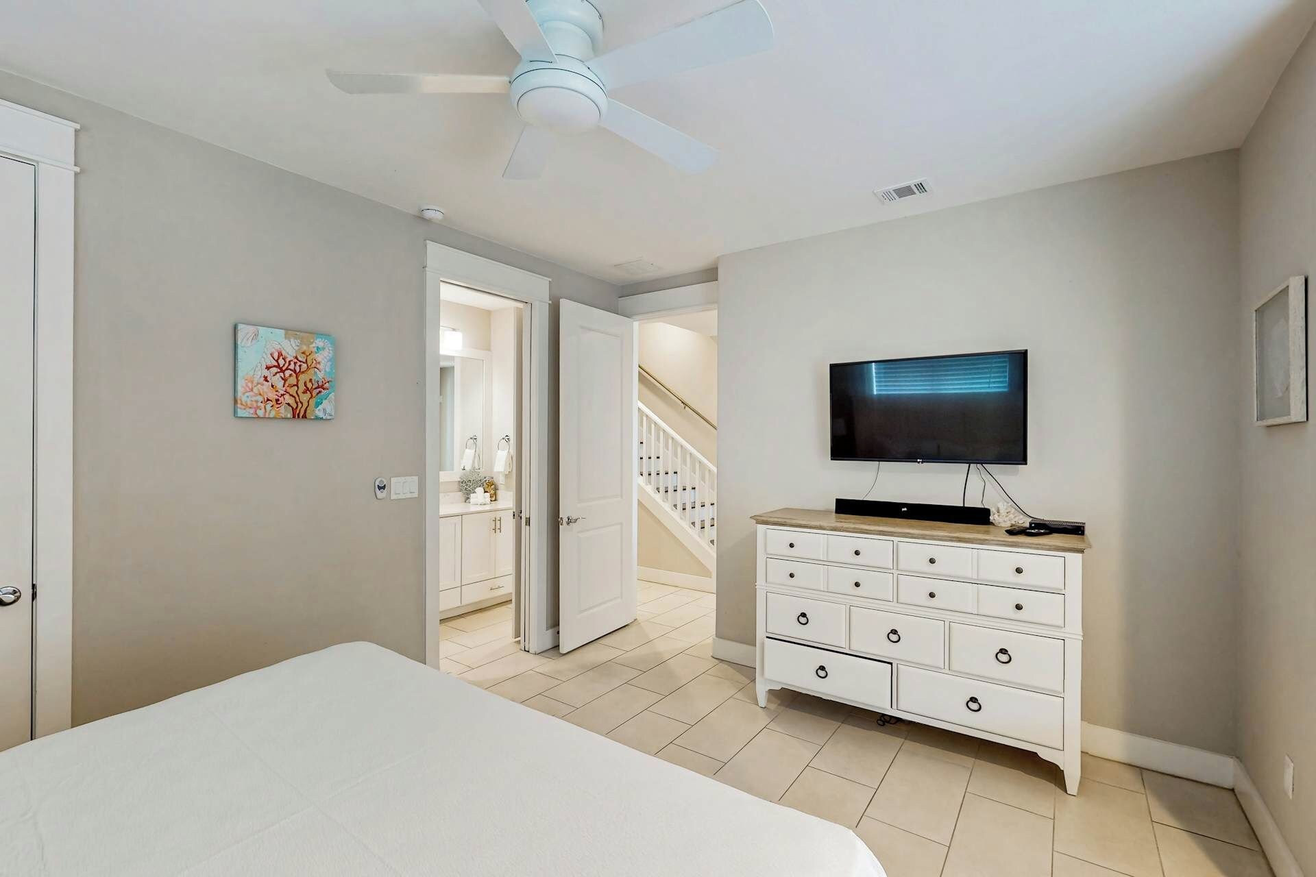 A bedroom with a bed, a dresser, a television, and a ceiling fan.
