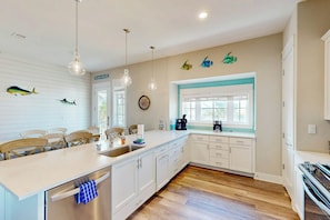 Una cocina con una isla grande, armarios blancos, un reloj y decoración de peces en la pared.