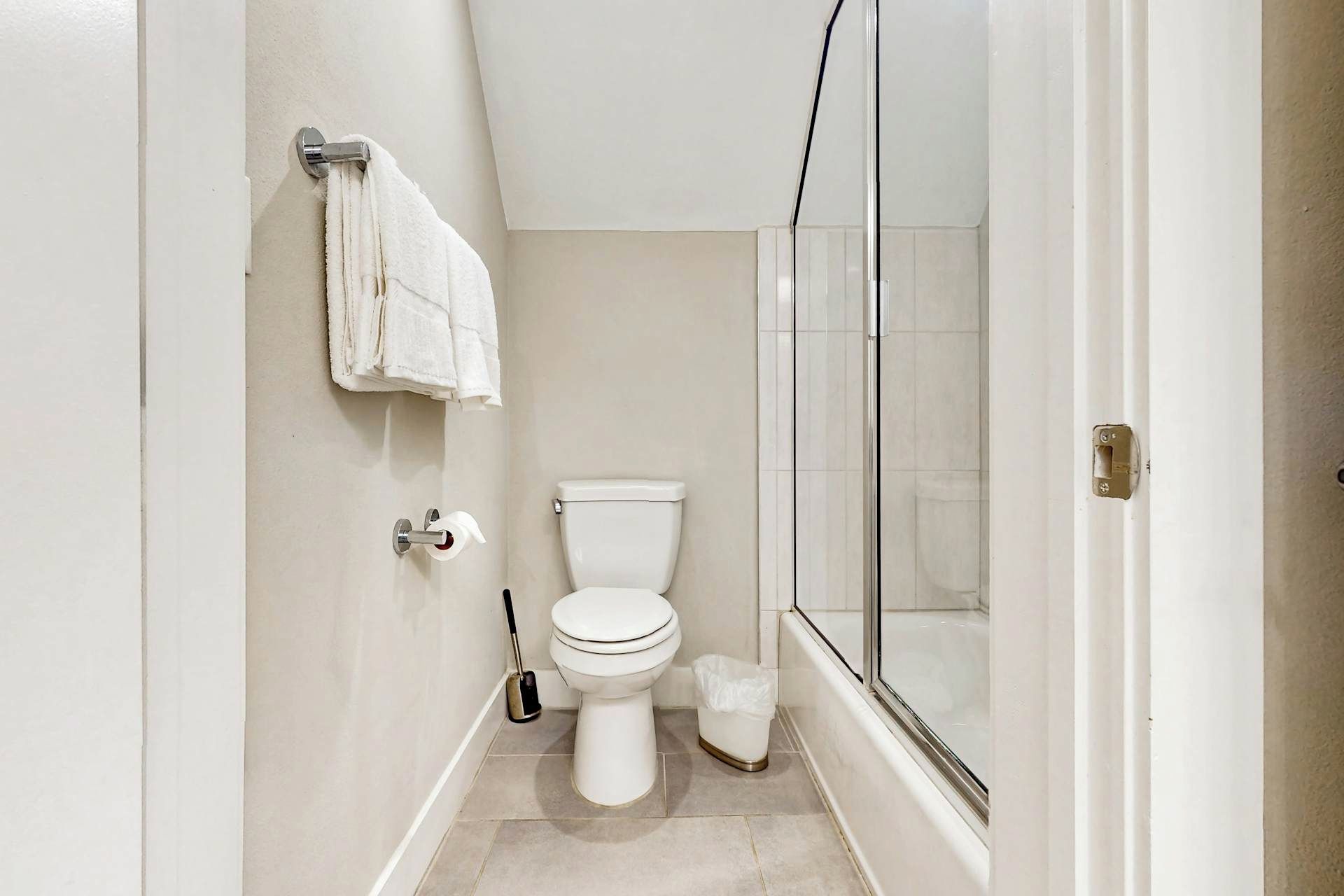 A compact bathroom with a toilet, a trash bin, a mop, and a glass shower enclosure.