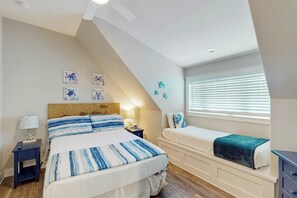 A bedroom with a bed, bedside tables, a window with blinds, and wall art. - Perfect Pelican | Resort Amenities| Beach Access (Port Aransas)