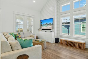 A living room with a sofa, a television, and a wicker coffee table. - Pines To Palms | Steps to Beach | Resort Amenities (Port Aransas)