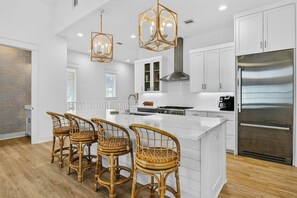 A modern kitchen with white cabinetry, a large island, and a stainless steel refrigerator. - Pines To Palms | Steps to Beach | Resort Amenities (Port Aransas)
