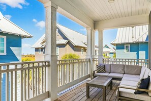 A covered outdoor area with a wooden deck, a sofa, and a table. - Pines To Palms | Steps to Beach | Resort Amenities (Port Aransas)