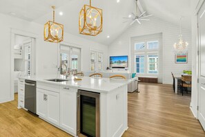 A spacious kitchen with a central island, white cabinetry, and a large window. - Pines To Palms | Steps to Beach | Resort Amenities (Port Aransas)