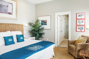 Quarto de hotel com cama, cadeira, planta e obras de arte nas paredes.