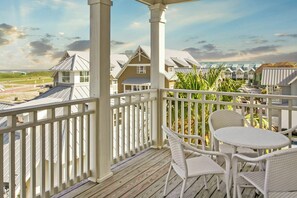 A wooden deck with white wicker furniture and a view of houses in the background. - Poolside Paradise | Gulf Views | Private Elevator (Port Aransas)
