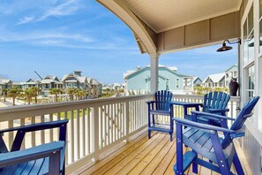 A wooden deck with blue Adirondack chairs, a white railing, and a view of beach houses. - Sabal By The Sea | Gulf Views | Steps to Beach (Port Aransas)