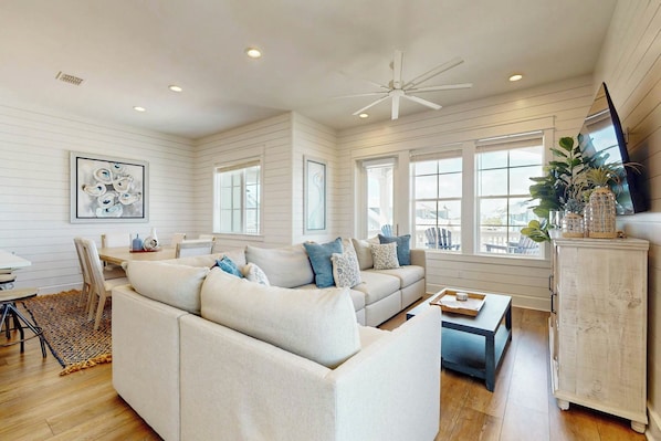 A living room with a sectional sofa, a coffee table, and a TV on a cabinet. - Sabal By The Sea | Gulf Views | Steps to Beach (Port Aransas)