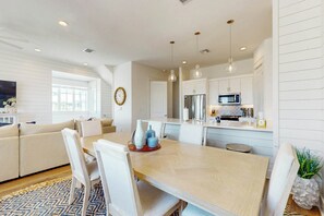A modern kitchen with white cabinetry, a dining table with chairs, and pendant lighting. - Sabal By The Sea | Gulf Views | Steps to Beach (Port Aransas)