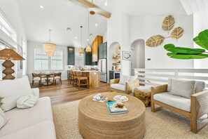 A spacious living area with a dining set, a round woven coffee table, and a seating area with a sofa and armchair. - Salt and Serenity | Steps to Beach | Game Room (Port Aransas)
