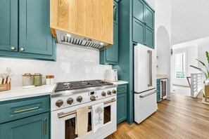A kitchen with teal cabinets, a stainless steel stove, and a white refrigerator. - Salt and Serenity | Steps to Beach | Game Room (Port Aransas)