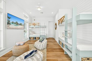 A room with bunk beds, a large window with a view, and a ceiling fan. - Salt and Serenity | Steps to Beach | Game Room (Port Aransas)