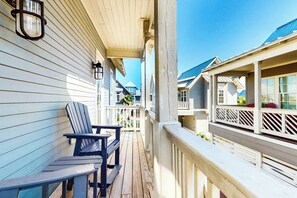 Um deck de madeira com duas cadeiras Adirondack, guarda-corpo e vista para casas vizinhas.