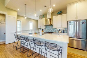 A modern kitchen with a central island, stainless steel appliances, and bar stools. - Sandy Toes | Golf Views | Pet Friendly (Port Aransas)
