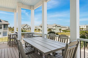 A covered outdoor area with a wooden table and chairs, overlooking a residential neighborhood. - Seaside Serenity | Resort Amenities (Port Aransas)