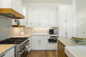 Eine moderne Küche mit weißen Schränken, einem Gasherd, einem Backofen, einer Mikrowelle und einer Kaffeemaschine.