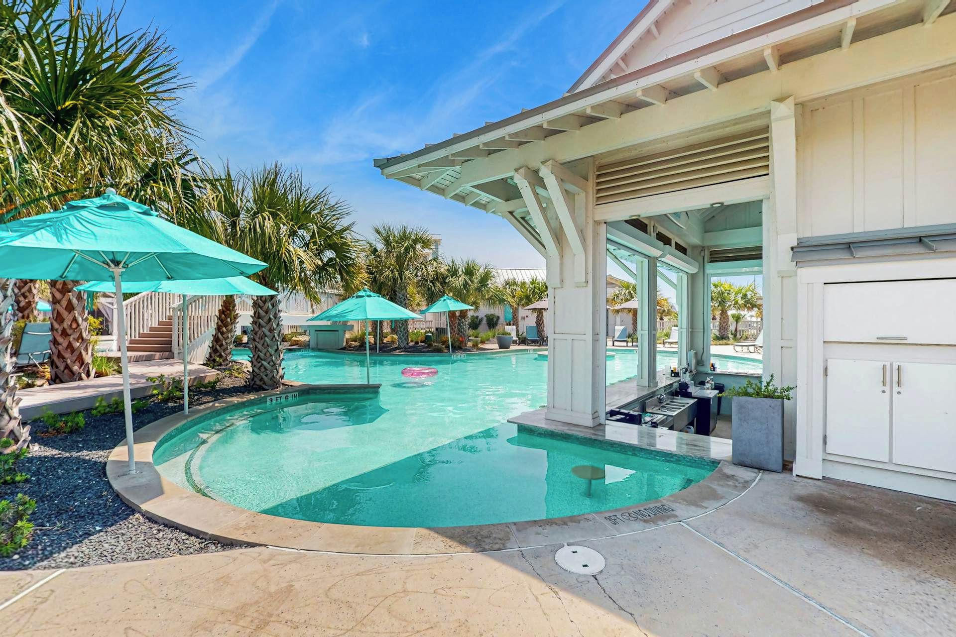 Un área de piscina con piscina circular, sillas de descanso y sombrillas.