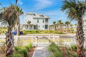 A two-story house with a balcony, surrounded by palm trees and a white picket fence. - Seaside Serenity | Resort Amenities (Port Aransas)