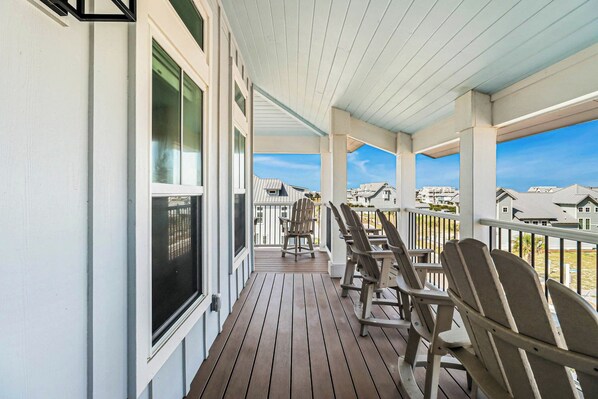 Eine überdachte Veranda mit Holzboden, weißen Geländern und Adirondack-Stühlen.