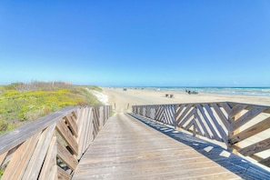 Une promenade en bois qui mène à une plage, avec un ciel dégagé.