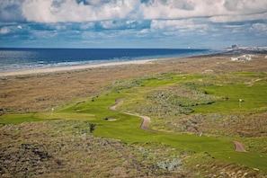 A golf course with a coastal view, a sandy beach, and a hilly landscape. - Serenity Now | Gulf Views | Steps to Beach (Port Aransas)