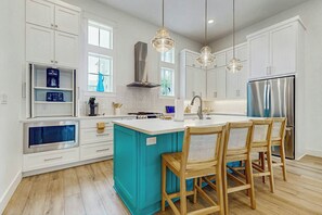 Une cuisine moderne avec des meubles blancs, un îlot central et un réfrigérateur en acier inoxydable.