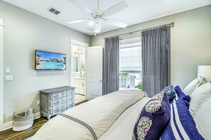 Ein Schlafzimmer mit Bett, Kommode, Fernseher und Blick ins Freie.