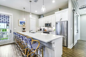 A modern kitchen with white cabinetry, stainless steel appliances, and a central island with bar stools. - Smiles And S'mores | Golf Views | Steps to Beach (Port Aransas)