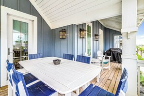 Un espace de restauration en plein air avec une table blanche et des chaises bleues, entouré d’une terrasse en bois et protégé par un auvent blanc.
