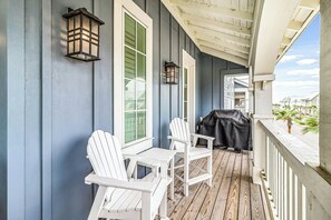 Eine überdachte Veranda mit Holzboden, weißen Adirondack-Stühlen und einem Grill.