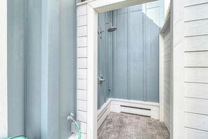A small, enclosed shower area with a door, a showerhead, and a hose. - Starfish Cottage | Water Views | Steps to Beach (Port Aransas)