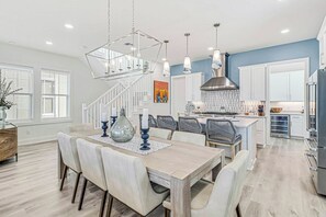 A modern kitchen with white cabinets, a stainless steel range hood, and a dining area with a wooden table and chairs. - Starfish Cottage | Water Views | Steps to Beach (Port Aransas)
