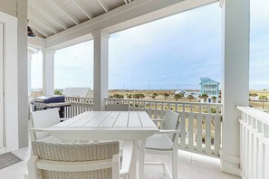 A covered outdoor seating area with a table and chairs, overlooking a beach and a building. - Sunrise to Sunset | Gulf Views | Steps to Beach (Port Aransas)