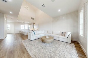 A spacious living area with a white sectional sofa, a round coffee table, and a kitchen in the background. - Sunrise to Sunset | Gulf Views | Steps to Beach (Port Aransas)
