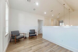A spacious room with a high ceiling, a wooden floor, two leather chairs, a small round table, and a large mirror above a white counter. - Sunrise to Sunset | Gulf Views | Steps to Beach (Port Aransas)