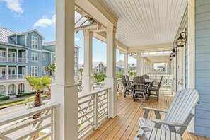 A covered outdoor deck with wooden furniture and a view of neighboring buildings. - Sunset Avenue Stunner | Steps to Beach (Port Aransas)