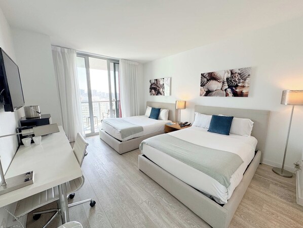 Une chambre d’hôtel avec deux lits, un bureau, une chaise, une télévision et des œuvres d’art accrochées aux murs.