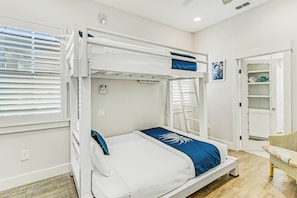 A bunk bed with a ladder, a bedside table, and a chair in a room with white walls and a wooden floor. - Poolside Luxury | Private Elevator (Port Aransas)